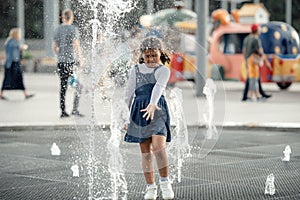 Little adorable girl have fun in street fountain at hot sunny day