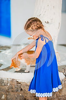 Little adorable girl playing with ginger cat in greek village outdoor