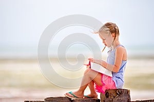 Little adorable girl reading book during tropical white beach