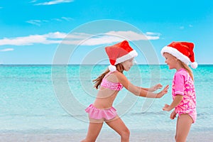 Little adorable girls in Santa hats during beach vacation have fun together