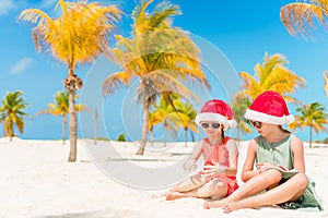 Little adorable girls in Santa hats during beach vacation have fun together