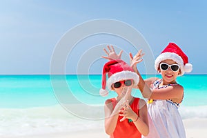 Little adorable girls in Santa hats during beach vacation have fun together