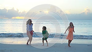 Little adorable girls and young mother at tropical beach in warm evening dancing and having fun. Family at sunset