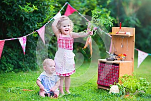 Little adorable kids playing with toy kitchen in the garden