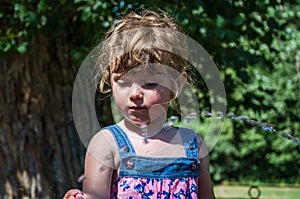 A little adorable little girl, a baby in a dress, drinks water from a spout of a Roman drinking fountain on a hot summer day, quen