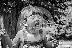 A little adorable little girl, a baby in a dress, drinks water from a spout of a Roman drinking fountain on a hot summer day, quen