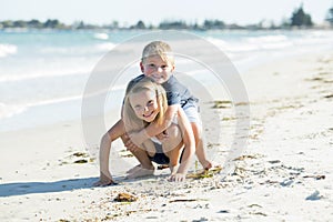 Little adorable and sweet siblings playing together in sand beach with small brother hugging his beautiful blond young sister enjo photo