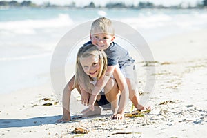 Little adorable and sweet siblings playing together in sand beach with small brother hugging his beautiful blond young sister enjo