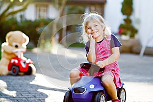 Little adorable toddler girl driving toy car and having fun with playing with plush toy bear, outdoors. Gorgeous happy