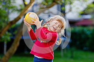 Little adorable toddler girl playing with ball outdoors. Happy smiling child catching and throwing, laughing and making