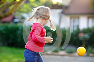 Little adorable toddler girl playing with ball outdoors. Happy smiling child catching and throwing, laughing and making