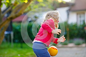 Little adorable toddler girl playing with ball outdoors. Happy smiling child catching and throwing, laughing and making