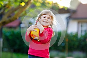 Little adorable toddler girl playing with ball outdoors. Happy smiling child catching and throwing, laughing and making