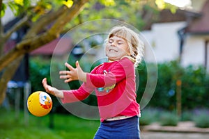 Little adorable toddler girl playing with ball outdoors. Happy smiling child catching and throwing, laughing and making