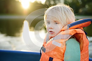 Little afraid boy boating on a river or pond at sunny summer day. Quality family time together on nature. Safety