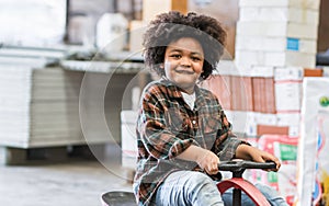 Little african afro hair boy wearing casual shirt, playing with happiness in warehouse or factory in holiday, riding bike or