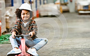 Little african afro hair boy wearing casual shirt and safety hat, playing with happiness in warehouse or factory in holiday,