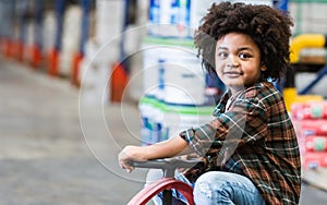 Little african afro hair boy wearing casual shirt and safety hat, playing with happiness in warehouse or factory in holiday,