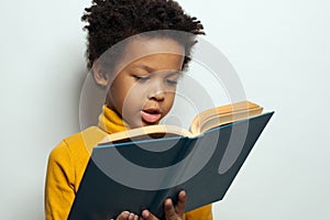 Little African American child boy reading a book on white background. Black kid student portrait