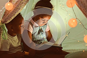 Little African-American children reading bedtime story in hovel