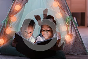 Little African-American children reading bedtime story in hovel photo