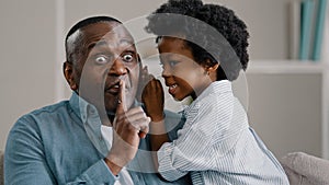 Little african american daughter whispering secret adult dad in ear telling gossip surprised dad carefully listens