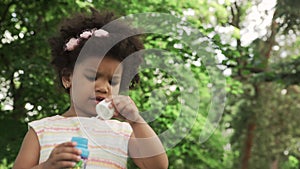 Little African-American girl blow soap bubbles in the park.