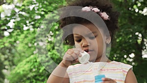 Little african-american girl blow soap bubbles in the park.
