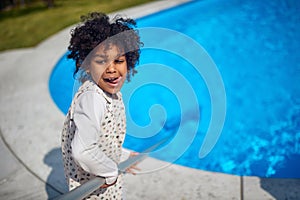 Little african american girl cleaning pool with cleaning net, standing by the pool and feeling happy