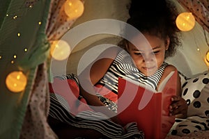 Little African-American girl reading bedtime story in hovel photo