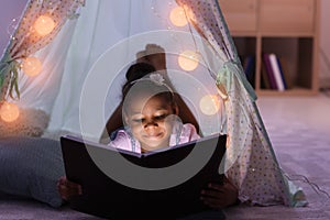 Little African-American girl reading bedtime story in hovel photo