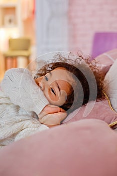 A little African American girl is sharing a bed in on a pink pillow. Vertical frame