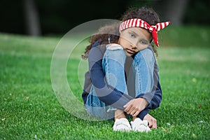Little african american girl sitting on green grass and looking at camera