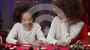 Little African American girl write a letter to Santa Claus and smile. Happy family portrait, New Years celebration