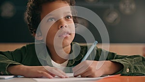 Little African American guy boy writing notes task class lesson primary school write in copybook kid schoolboy son child