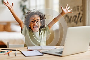 Little african american school boy raising hands up with excitement during home distance education