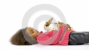 Little african curly girl lies on the floor with three colored rabbit at white background. Slow motion