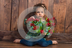 Little african girl in rural shirt with bunch of berries. Background of brown wooden wall