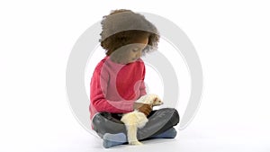 Little african girl is stroking albinos ferret furo with red eyes at white background. Close up. Slow motion