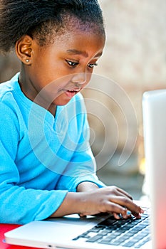 Little african girl typing on laptop.