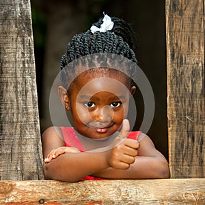 Little african girl at wooden fence with thumbs up.