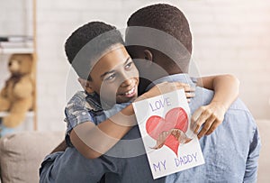 Little afro boy hugging dad and giving him handmade postcard