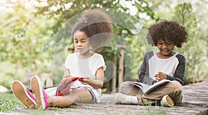 Little Afro child girl reading book between green spikes meadow garden with friend