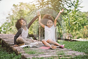 Little Afro child girl reading book between green spikes meadow garden with friend