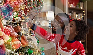 Little afro girl helping daddy to decorate family Christmas tree