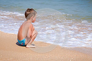 Little alone boy sitting on the beach near water