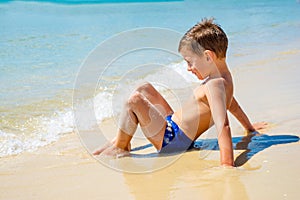 Little alone boy sitting on beach near water