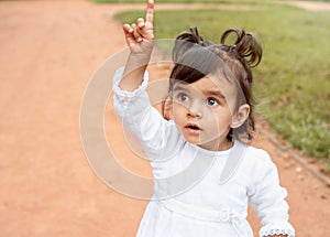 Little amazed baby girl pointing finger up in the park