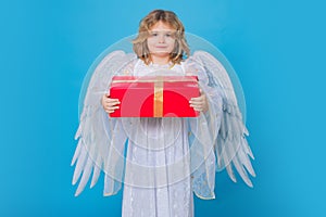 Little angel with gift box present. Valentine's day. Blonde cute child with angel wings on a blue isolated studio
