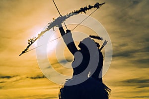 Little angel girl against sunny sky. Teen angel girl archer on sunset. Silhouette of a cupid. Side view of teen girl